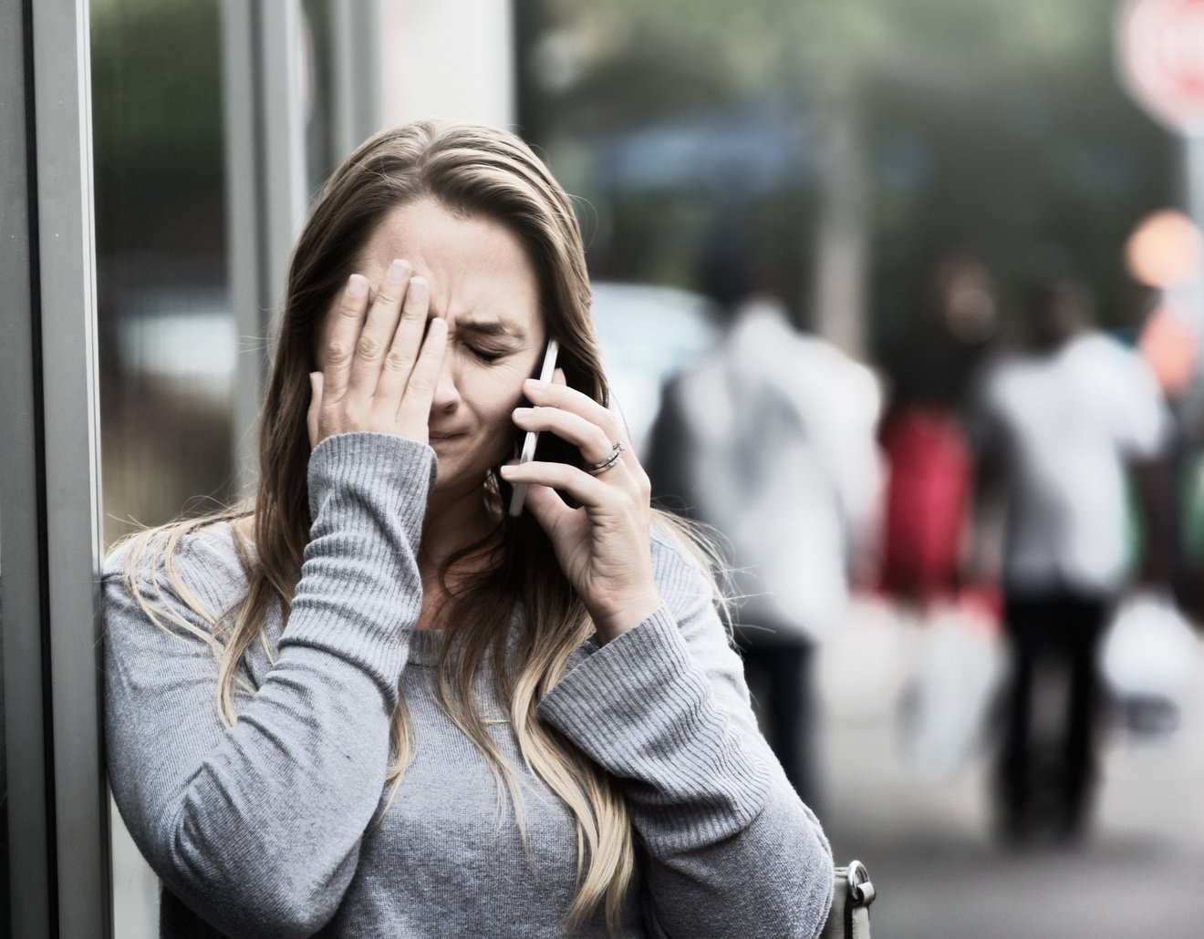 Crying woman talks on phone in street, distressed